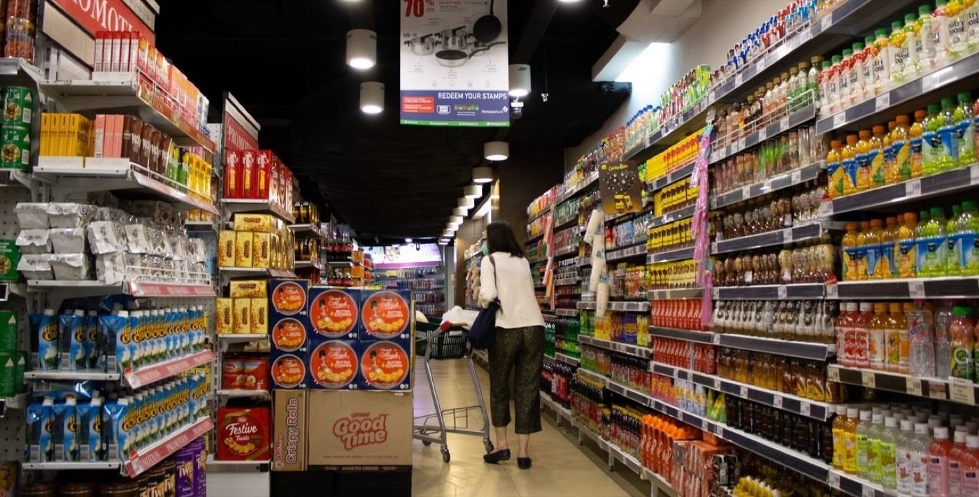 Lorong minimarket dengan rak penuh produk